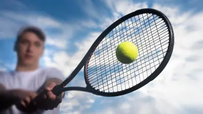 Close up of a person hitting a tennis ball with a tennis racquet and a blue sky in the background.