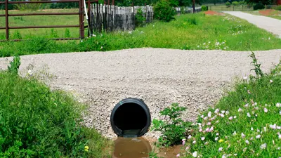 Photo of the end of a gravel driveway with a culvert under it to allow water from the ditch to flow.