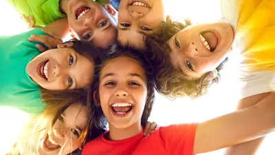 Smiling youth in a tight circle with their heads together, looking down towards the camera.