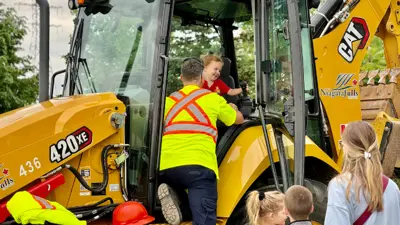 City of Niagara Falls employee helping a young child sit inside a parked construction vehicle during the Touch A Truck event.