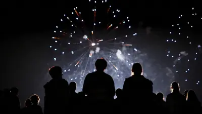 A silhouette of a group of people watching fireworks in the sky at night.